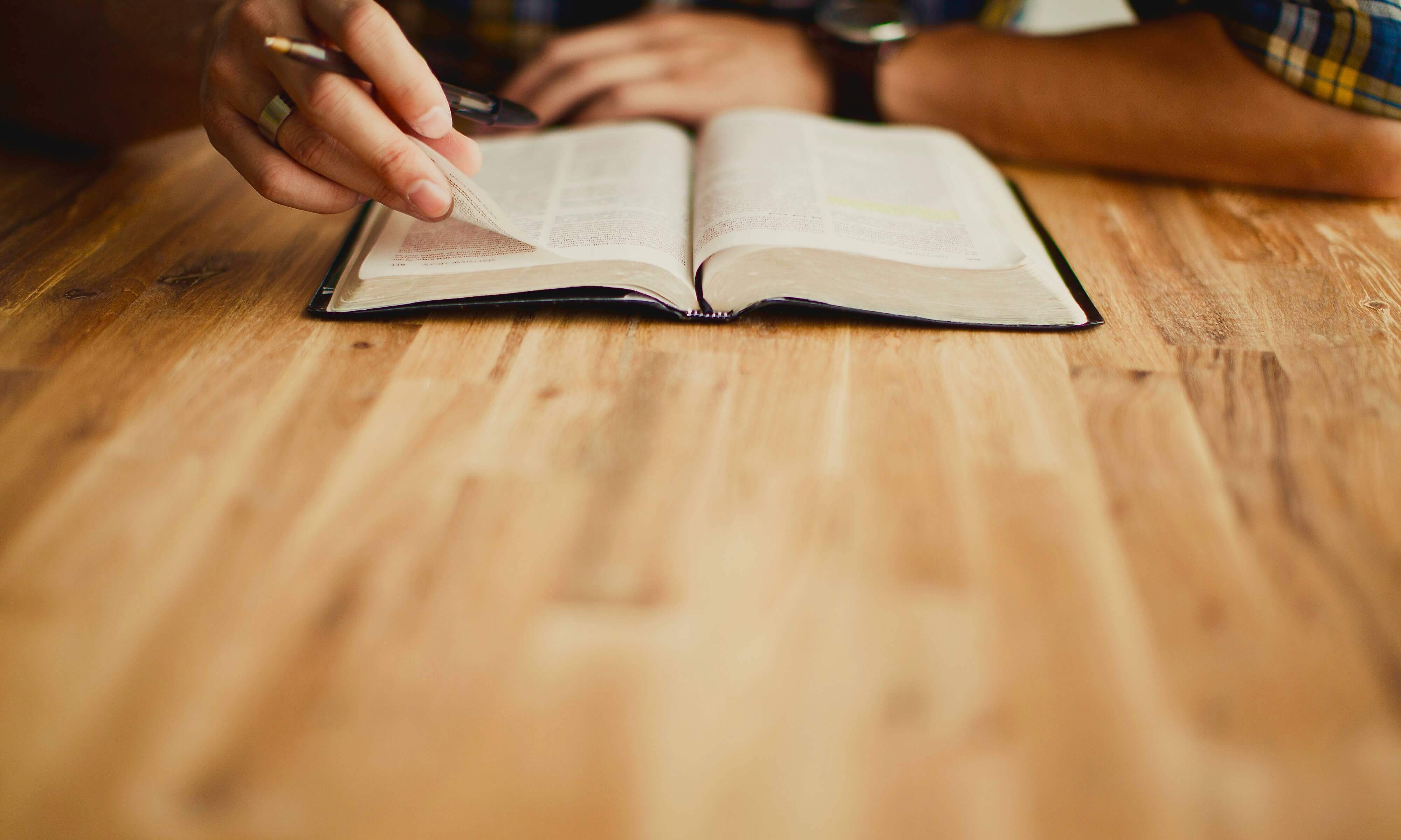 a hand holding a page in a bible and a pen as the person reads